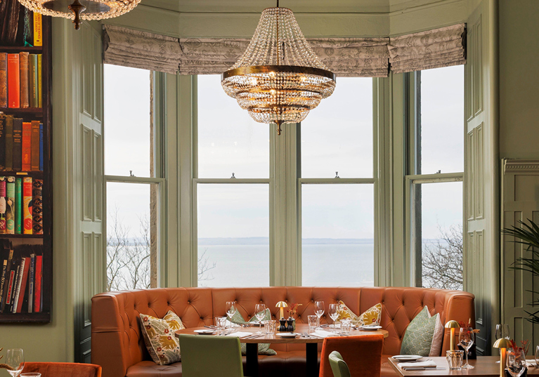 Hotel du Vin St Andrews' Bistro, with green walls and burnt orange plush seating, including a bookcase to the left.