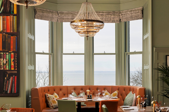 Hotel du Vin St Andrews' Bistro, with green walls and burnt orange plush seating, including a bookcase to the left.