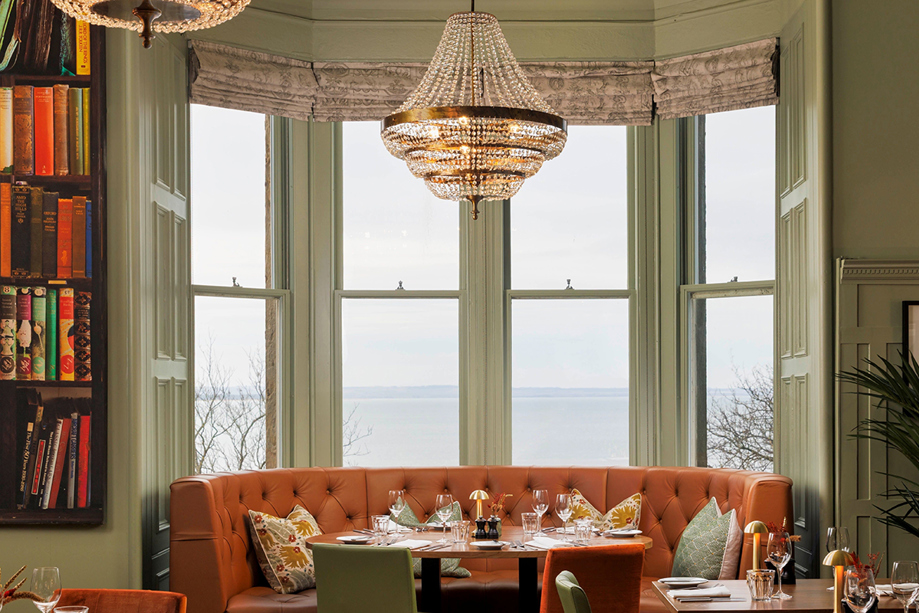 Hotel du Vin St Andrews' Bistro, with green walls and burnt orange plush seating, including a bookcase to the left.
