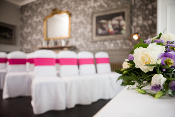 Wedding ceremony set up at Hotel du Vin St Andrews with hot pink chair bows and cream and purple bouquet in foreground.