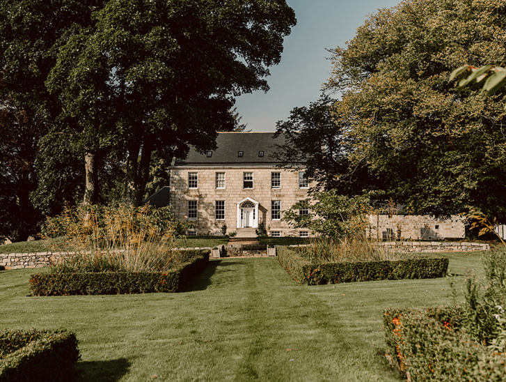Exterior of country house wedding venue, House of Elrick, on Elrick Estate in Aberdeenshire. Blue skies in background and lush manicured gardens in foreground.