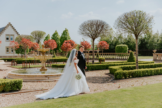 Bride and groom walking through manicured gardens at Ingliston Estate and Country Club wedding venue in Scotland