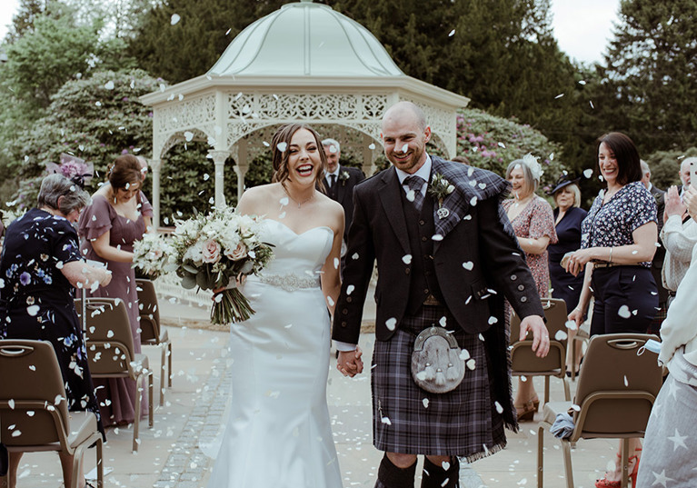 Bride and groom smile as they walk through confetti