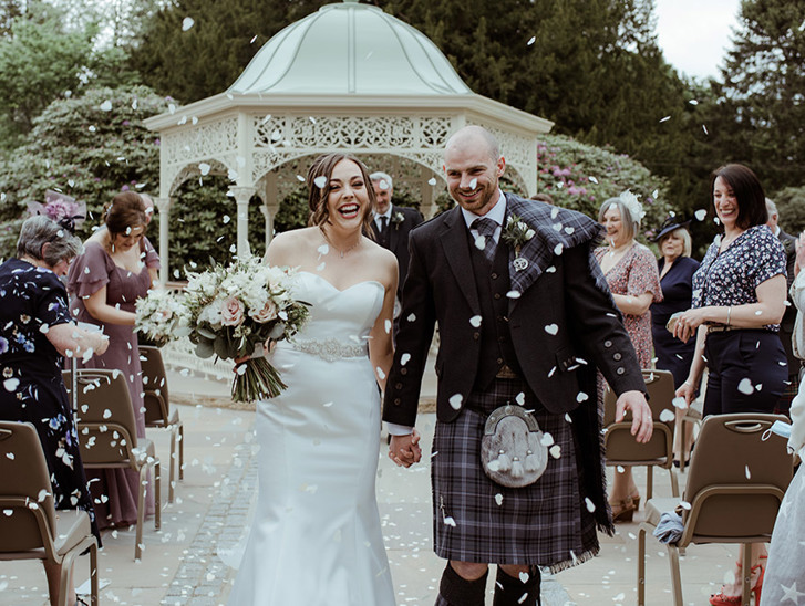 Bride and groom smile as they walk through confetti