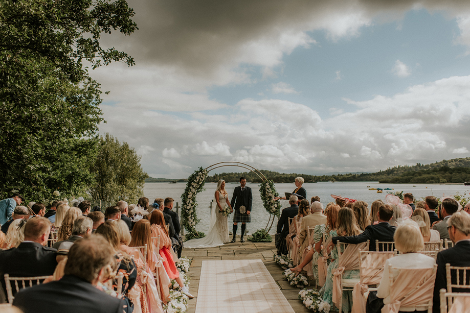 Bride and groom at altar for outdoor ceremony at Lodge on Loch Lomond with blue and cloudy skies.