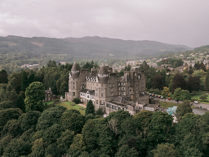 View of Atholl Palace Hotel from above with a drone, displaying its surrounding woodlands and hills in background of Pitlochry.