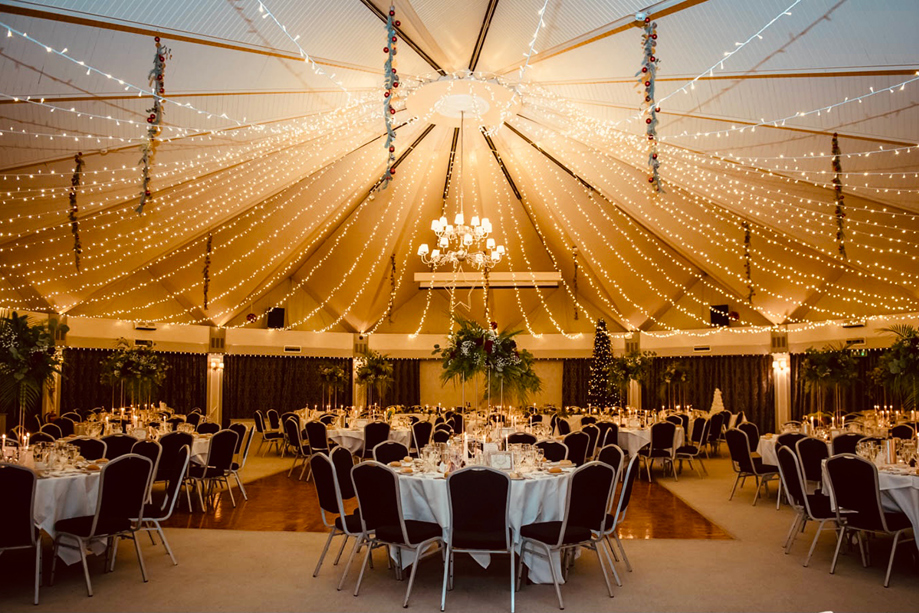Elegant wedding reception venue decorated with fairy lights, round tables, and floral centrepieces inside the grand marquee-style Atholl Suite at Atholl Palace Hotel in the Scottish Highlands.