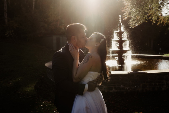 Bride and groom kissing in front of a sunlit outdoor fountain during their wedding photoshoot at Atholl Palace Hotel in Pitlochry.