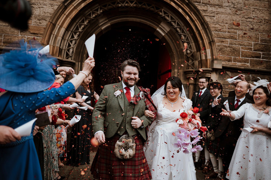 Bride and groom walking out of Mansfield Traquair through red confetti