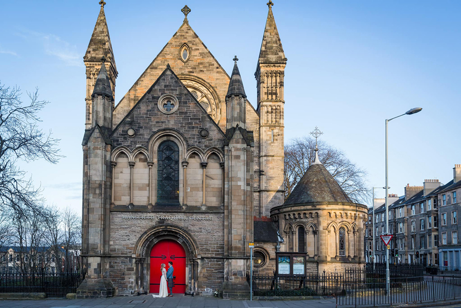 Couple look at each other outside red doors of Mansfield Traquair