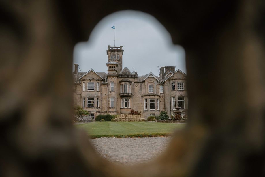 Auchen Castle exterior framed through a stone archway with garden ceremony chairs outside.