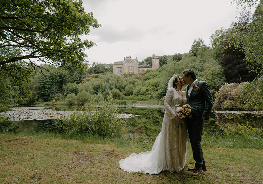 Bride and groom kiss on the grass with Auchen Castle in background