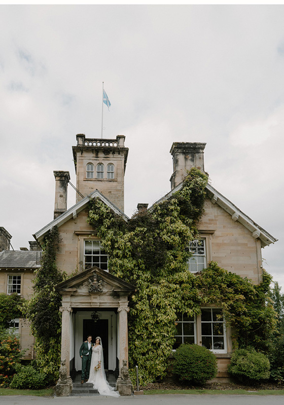 Bride and groom at door of Auchen Castle with turret and Scottish flag in view