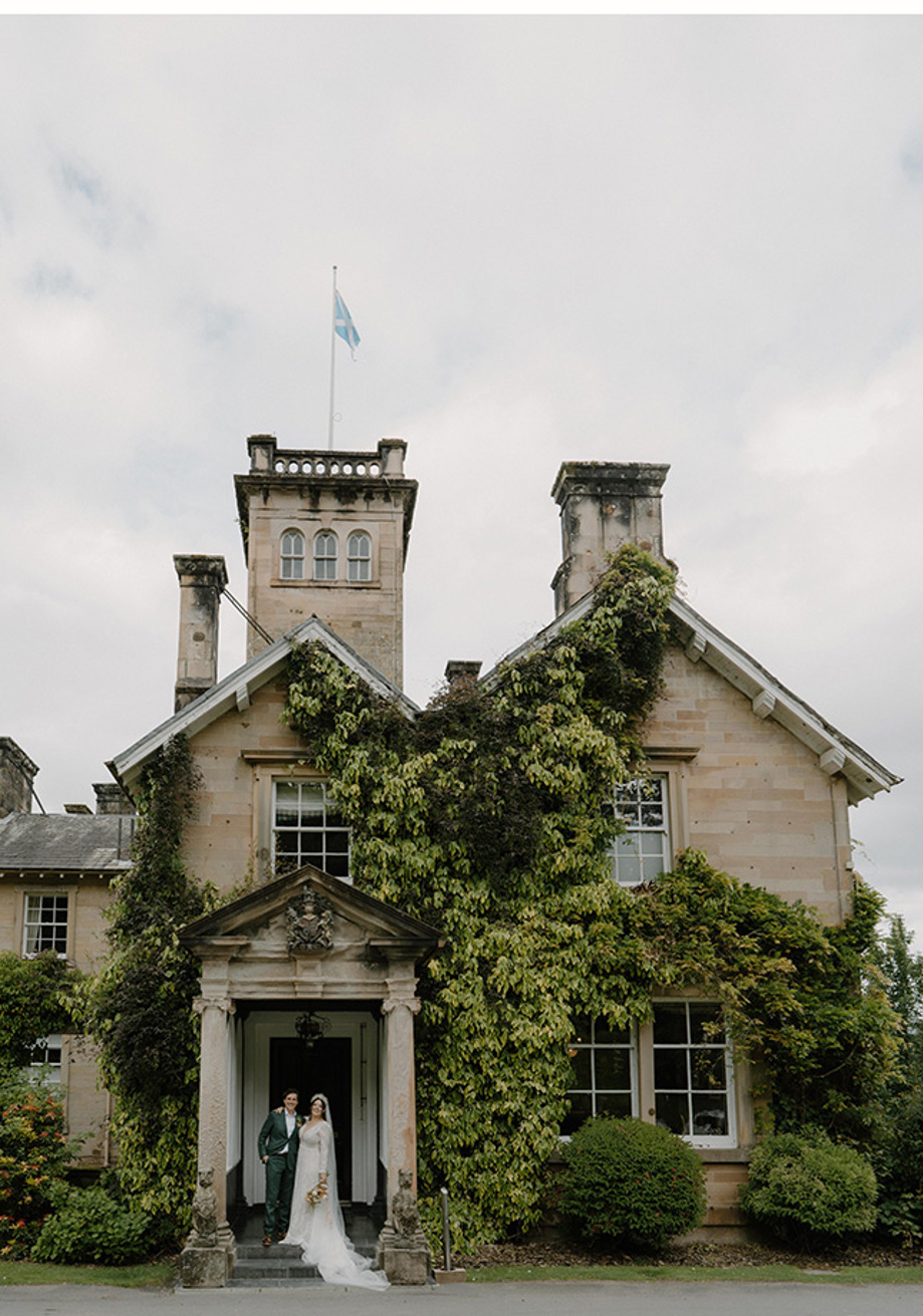 Bride and groom at door of Auchen Castle with turret and Scottish flag in view