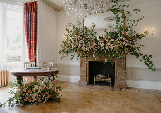 Registry table with two seats and fireplace decorated with huge leaves and orange and white flowers