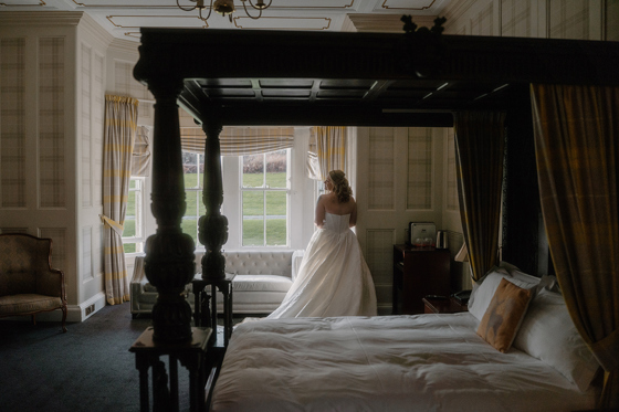 Bride standing by a window in an elegant bedroom at Auchen Castle before her wedding ceremony.