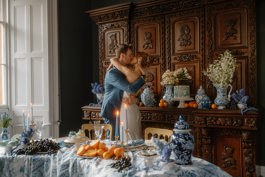 Couple kissing beside a blue and orange wedding tablescape inside Auchen Castle.