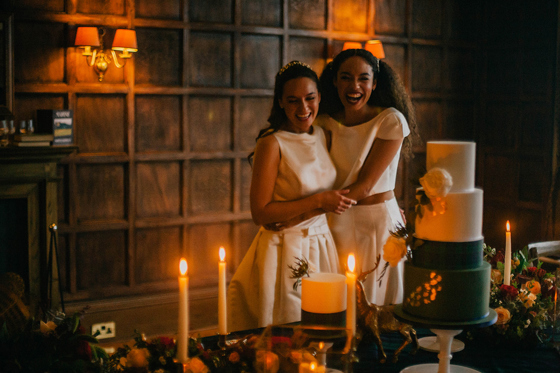 Two brides laughing beside a wedding cake at Marine North Berwick during evening reception celebrations