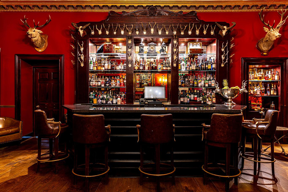 Traditional bar interior at Melville Castle with red walls, leather chairs and stag head decor.