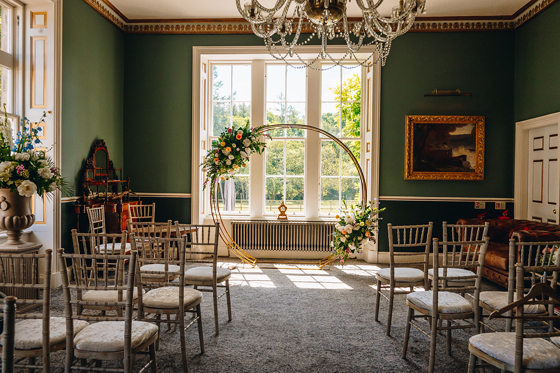 Indoor ceremony setup at Melville Castle with gold floral hoop, chandeliers and Chiavari chairs.
