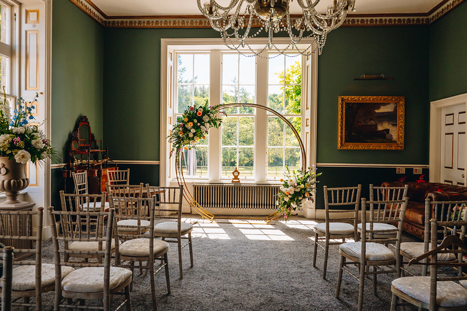 Indoor ceremony setup at Melville Castle with gold floral hoop, chandeliers and Chiavari chairs.