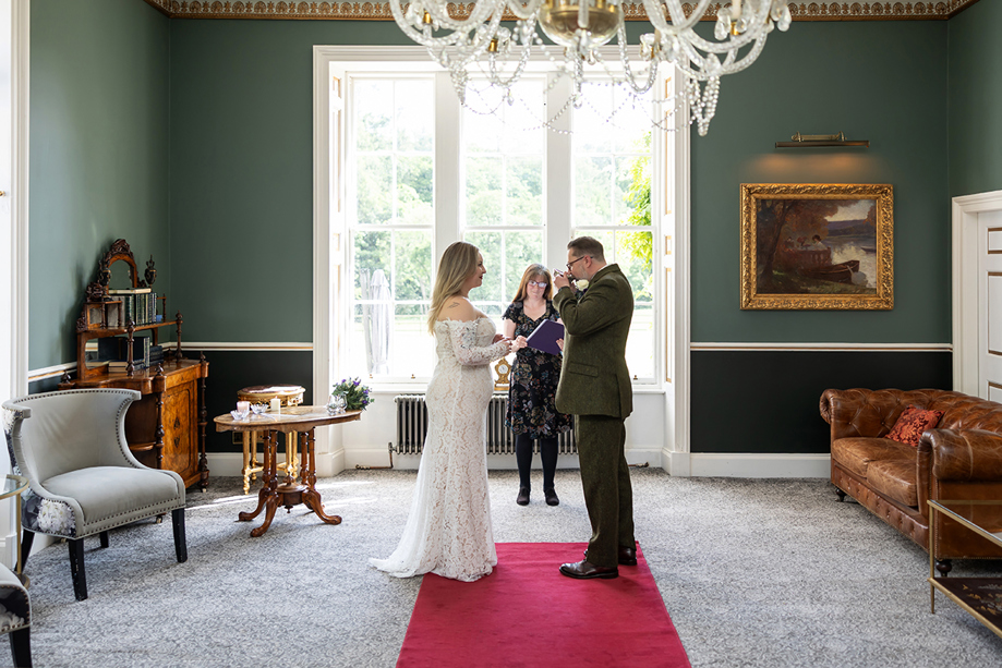 Intimate indoor wedding ceremony at Melville Castle with a couple exchanging vows in a green room.