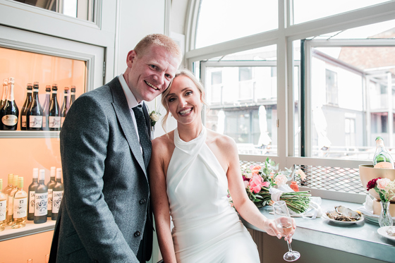 Bride and groom pose at window in BAaD in the Glasgow Barra's, with wine cooler in background.