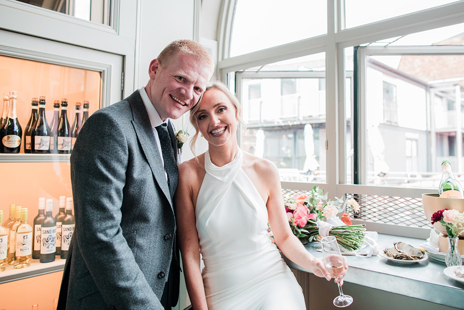 Bride and groom pose at window in BAaD in the Glasgow Barra's, with wine cooler in background.