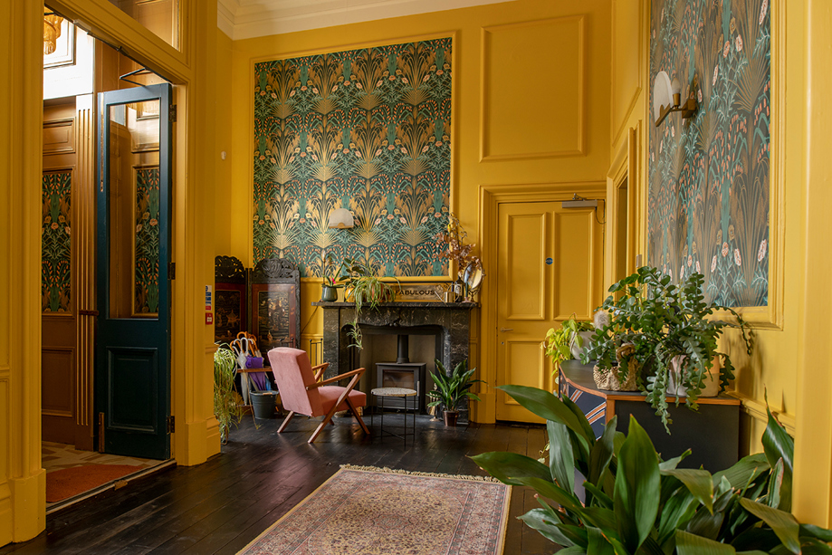 Entrance hall at Netherbyres House featuring mustard walls, botanical wallpaper, statement prints and indoor plants