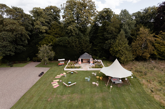 Drone view of outdoor wedding reception at Netherbyres House with stretch tent marquee, garden seating and woodland backdrop