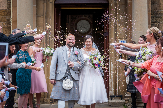 Bride and groom walking through confetti outside Newbattle Abbey College wedding entrance in Scotland