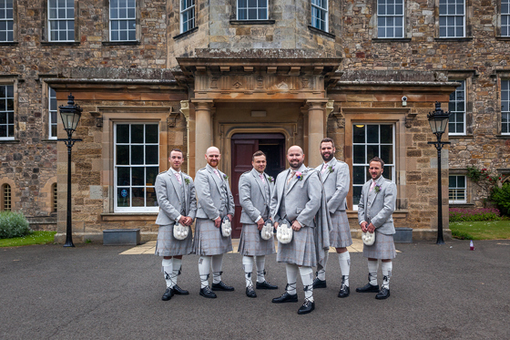 Groom and groomsmen in kilts outside Newbattle Abbey College historic wedding venue entrance
