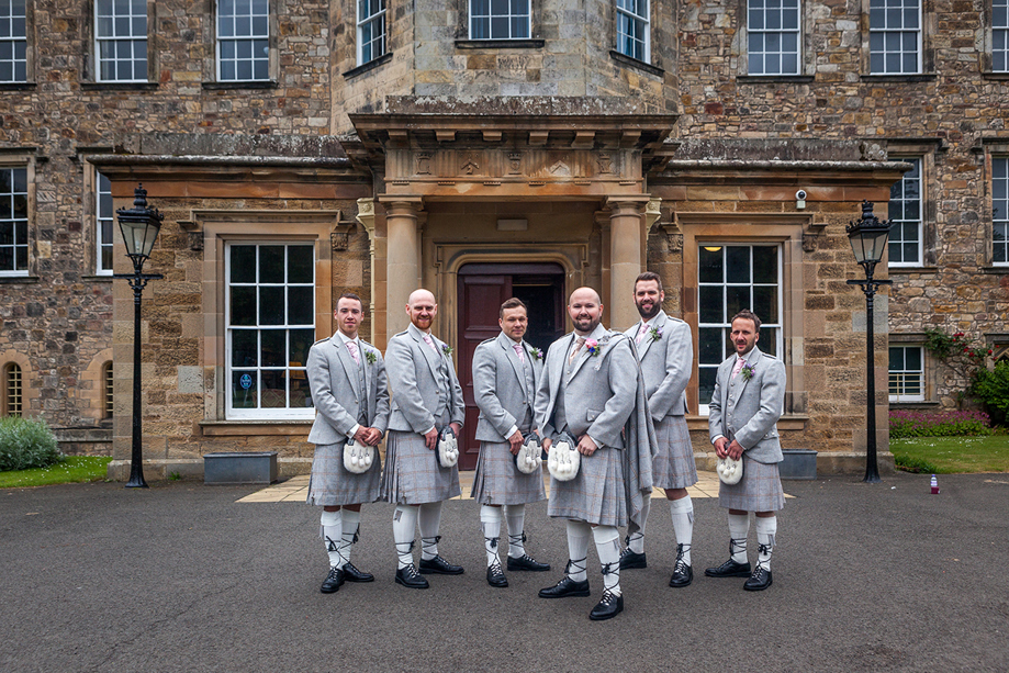 Groom and groomsmen in kilts outside Newbattle Abbey College historic wedding venue entrance