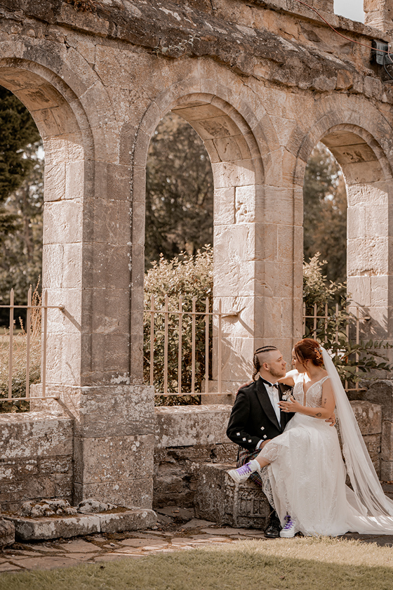 Wedding couple portrait at Newbattle Abbey College beside stone arches and landscaped gardens