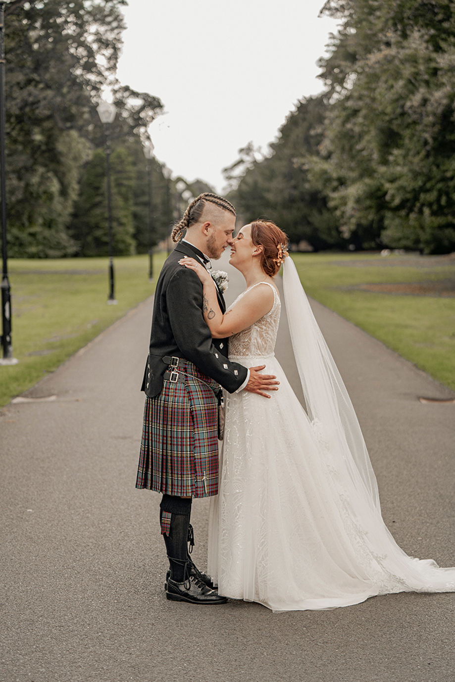 Wedding couple kissing on tree-lined driveway at Newbattle Abbey College in Scotland