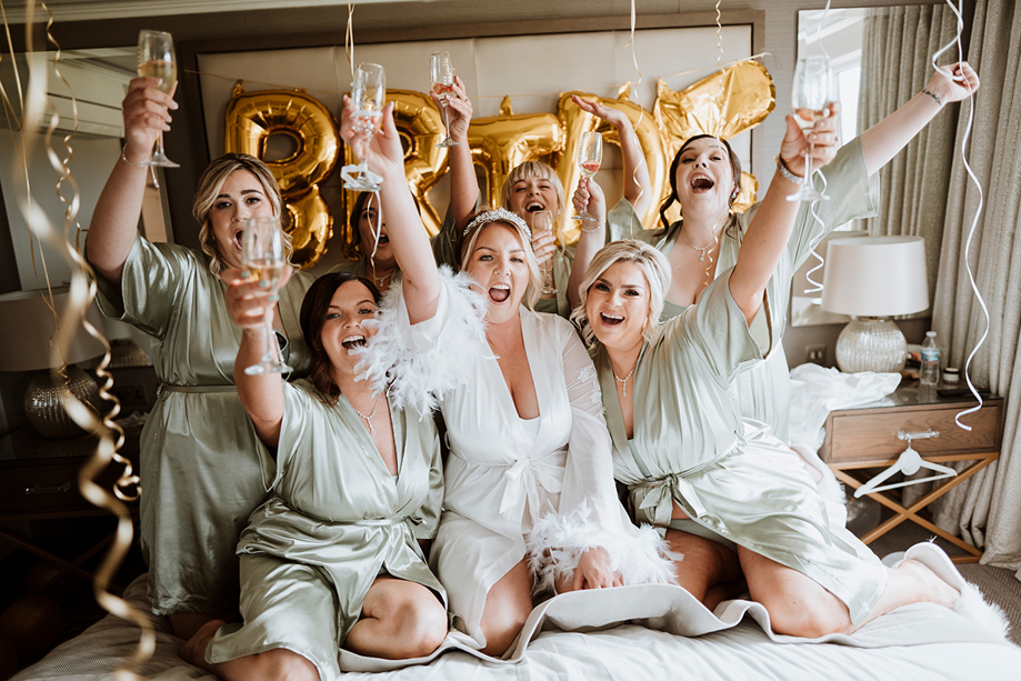 Bridal party celebrating on bed with gold "bride" balloons in background