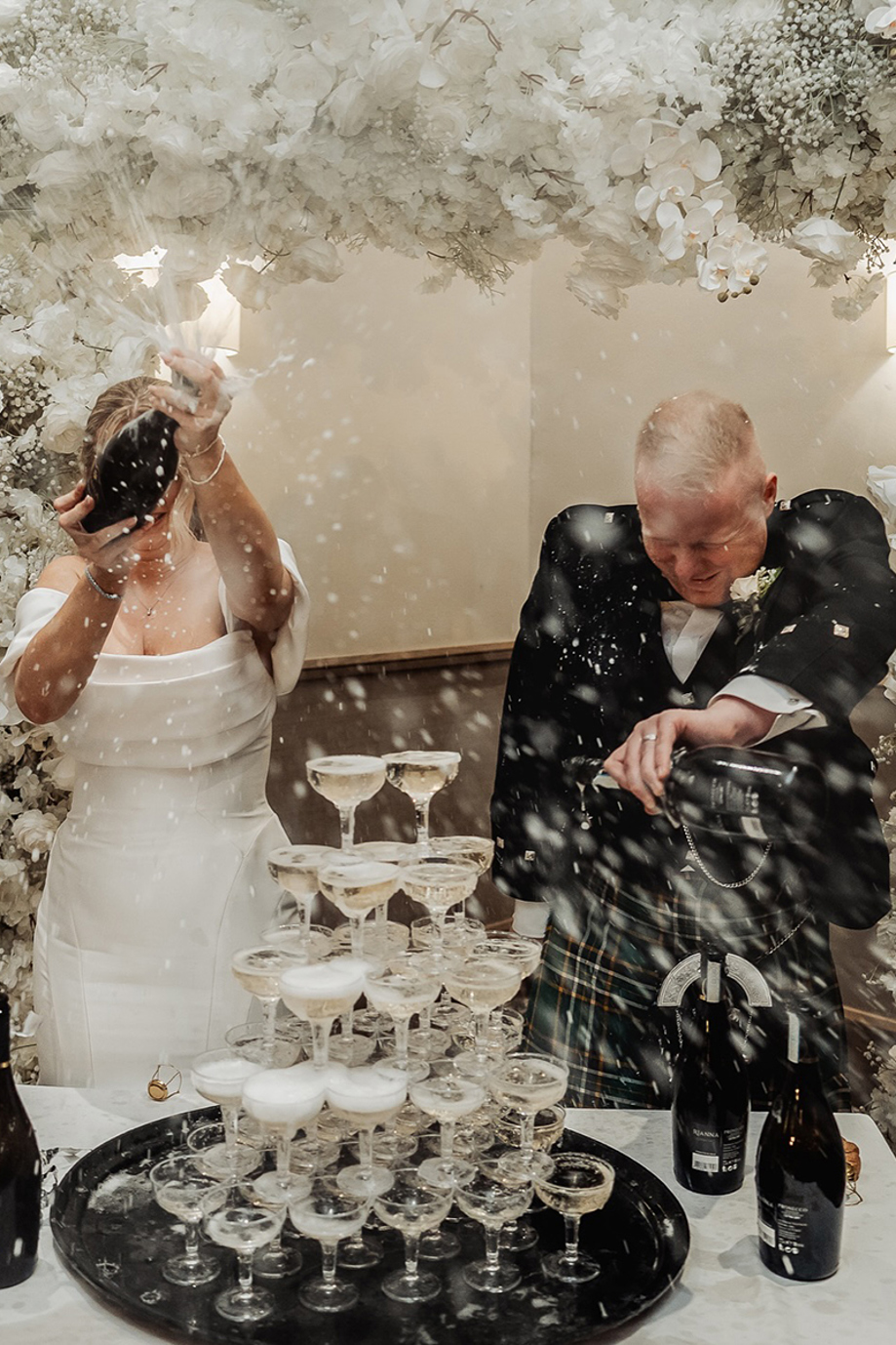 Bride and groom hide from champagne spray when pouring onto champagne tower