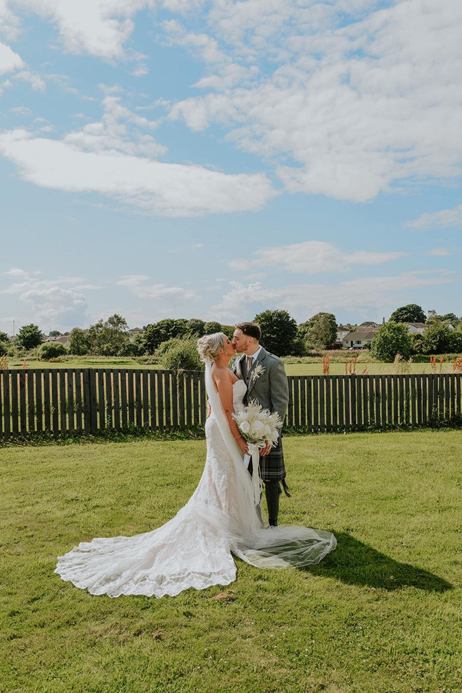 Bride and groom on grass at Riverside Lodge Hotel with blue skies in background