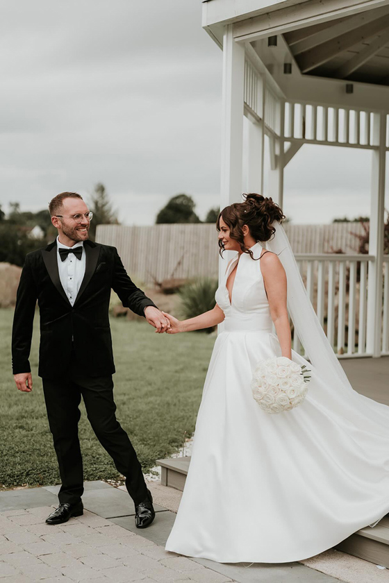 Groom helps bride down stairs on grounds of Riverside Lodge Hotel