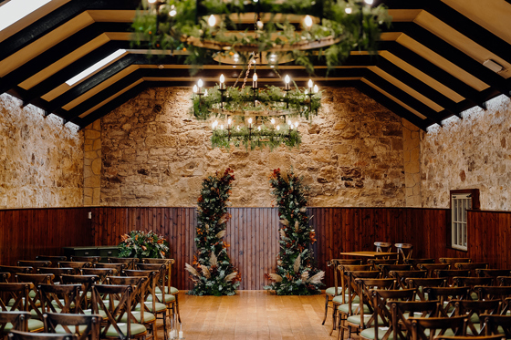 Rustic stone ceremony room with floral styling and candle chandeliers at Rosebery House wedding venue