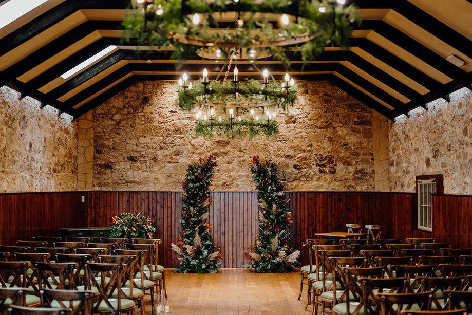 Rustic stone ceremony room with floral styling and candle chandeliers at Rosebery House wedding venue