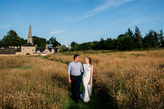 Couple walking through wildflower meadow with Rosebery House wedding venue in the background