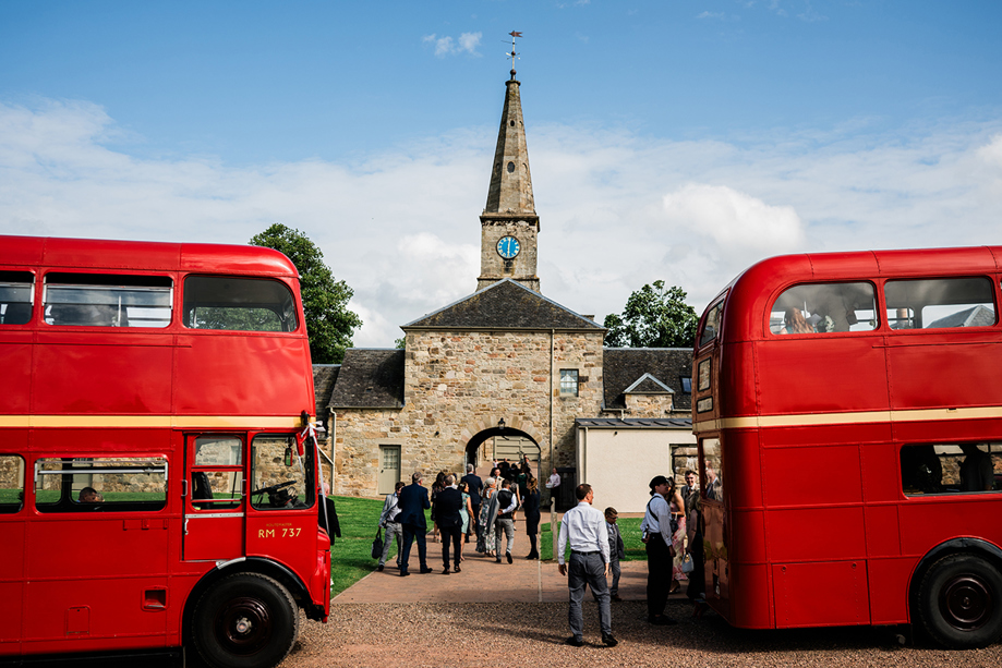 Guests arriving at Rosebery House wedding venue beside red vintage double decker buses