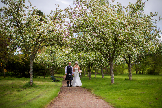 Bride and groom walk tree-lined path on the grounds of SCHLOSS Roxburghe in Kelso, captured by Parris Photography.