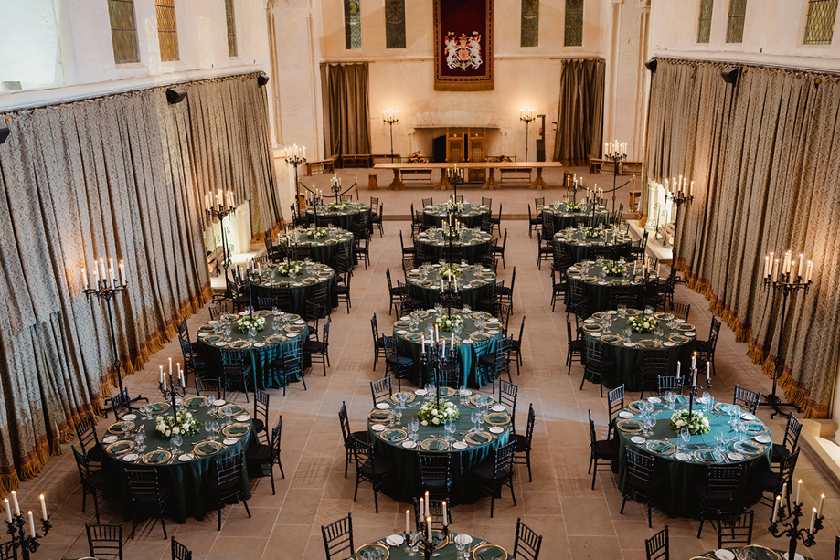 Stirling Castle Great Hall wedding reception setup with round tables, black Chiavari chairs and candlelit candelabras beneath historic vaulted ceiling.