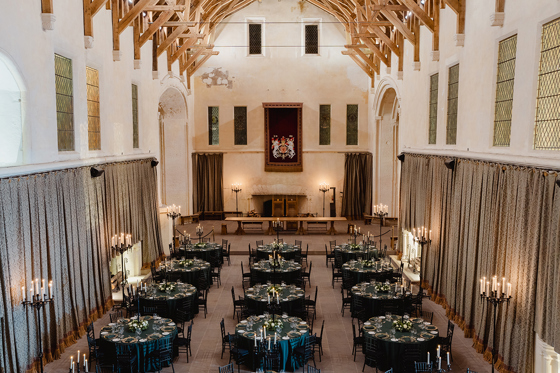 Overhead view of Stirling Castle Great Hall set for a luxury wedding dinner with dark green table linens, round tables and elegant candlelight.