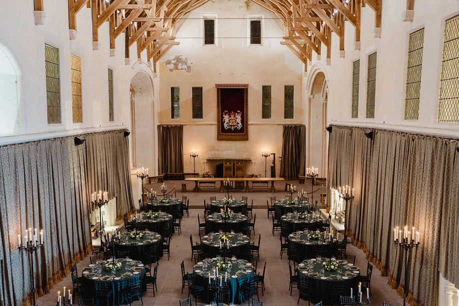 Overhead view of Stirling Castle Great Hall set for a luxury wedding dinner with dark green table linens, round tables and elegant candlelight.