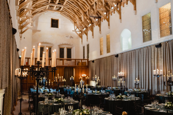 Wedding reception at Stirling Castle Great Hall featuring long candelabras, round banquet tables and dramatic medieval architecture.