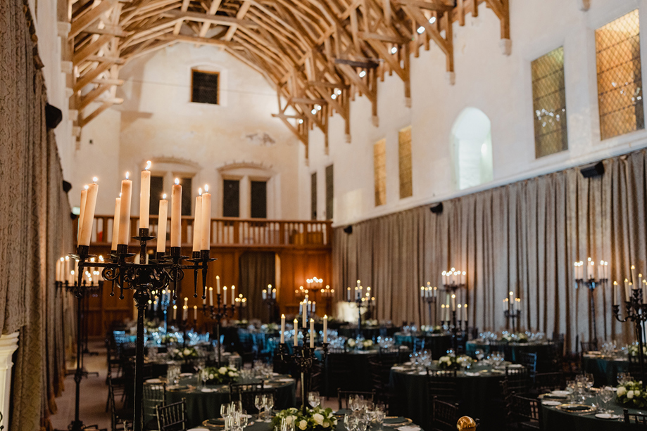 Wedding reception at Stirling Castle Great Hall featuring long candelabras, round banquet tables and dramatic medieval architecture.