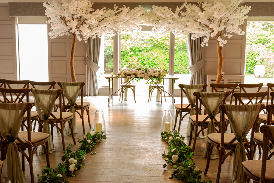 Wedding ceremony setup at Strathaven Hotel with floral arch, greenery-lined aisle and elegant indoor ceremony space.